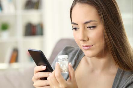 woman holding bottle of medicine looks up pharmaceuticals information on her smartphone