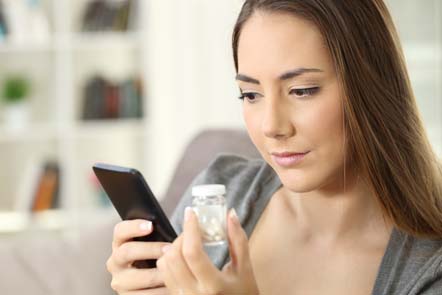 woman holding bottle of medicine looks up pharmaceuticals information on her smartphone